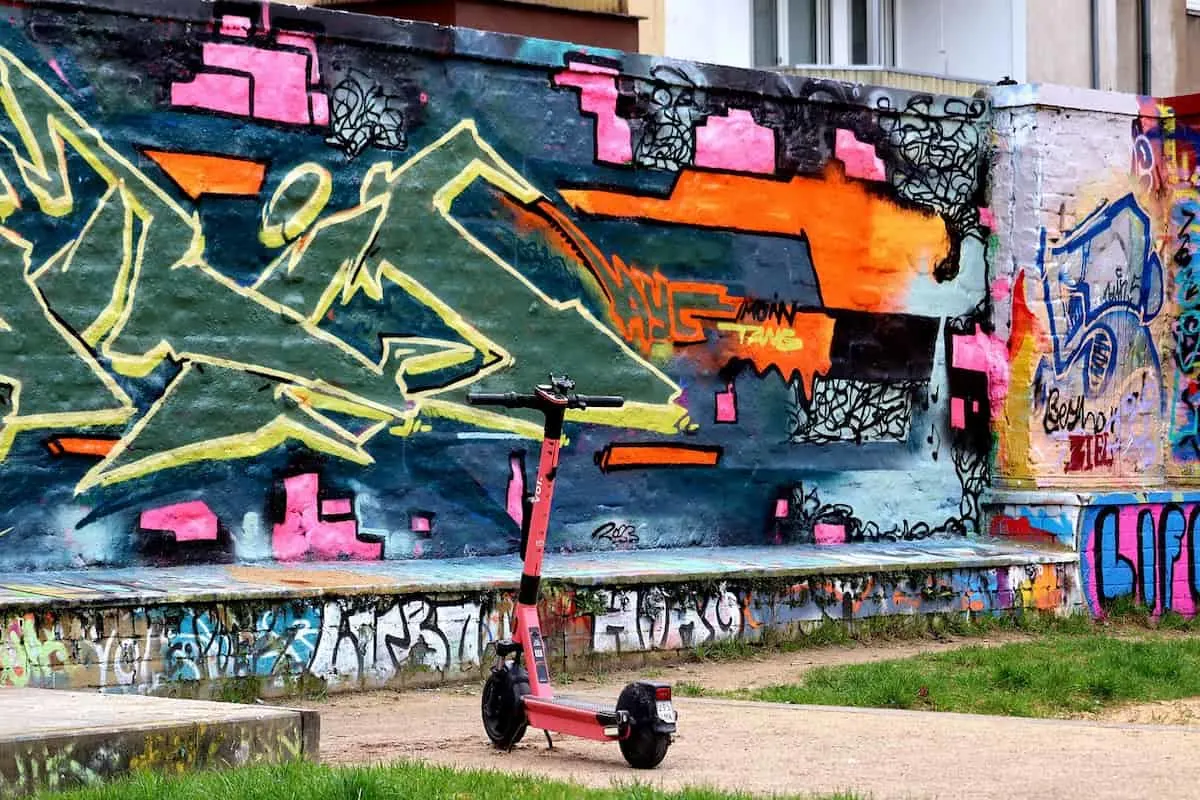 Patinete eléctrico rosa aparcado frente a un mural de graffiti colorido.
