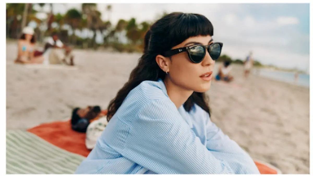 Mujer joven con gafas de sol Ray-Ban Meta sentada en la playa en un día de verano