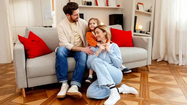 Familia de tres personas sentada en un sofá gris en el salón de su casa.