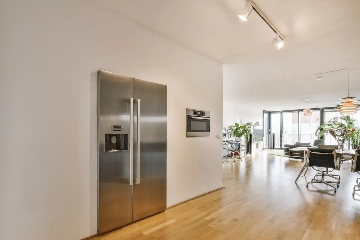 Frigorífico americano de acero inoxidable integrado en una cocina comedor moderna y luminosa de planta abierta.