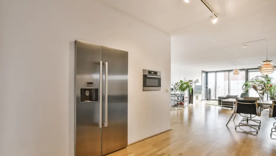 Frigorífico americano de acero inoxidable integrado en una cocina comedor moderna y luminosa de planta abierta.