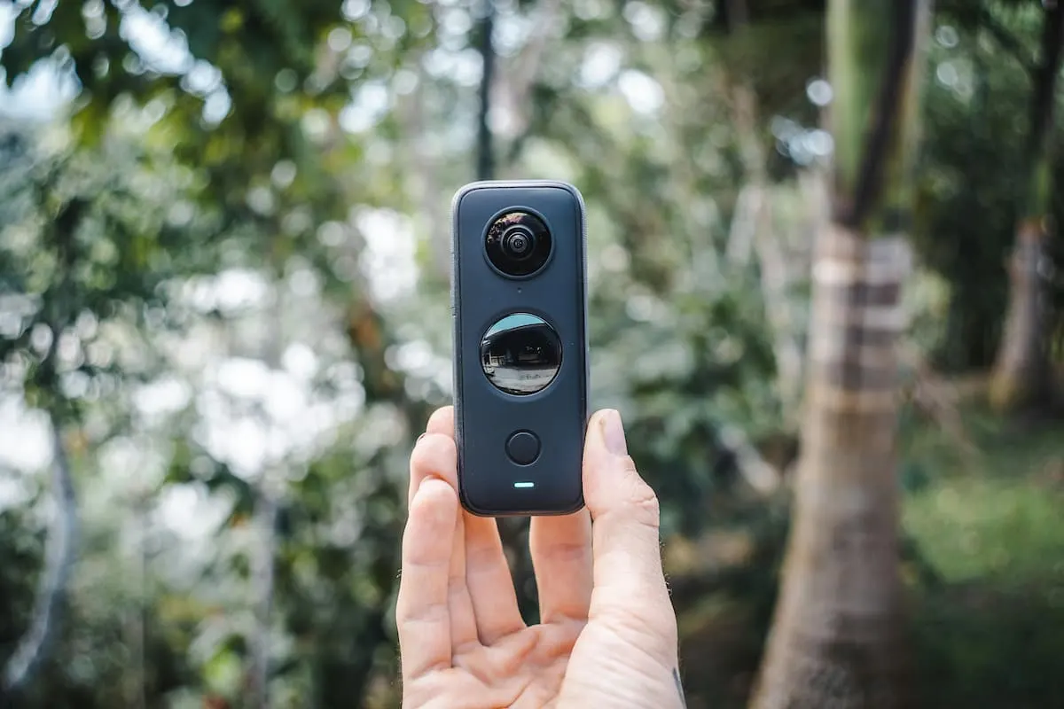 Mano sosteniendo una cámara 360 en medio de un bosque.