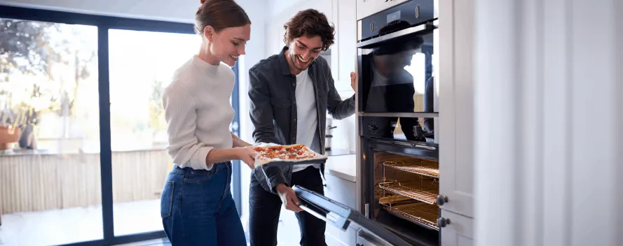 Una mujer y un hombre ponen pizza en un horno en una cocina moderna y luminosa.
