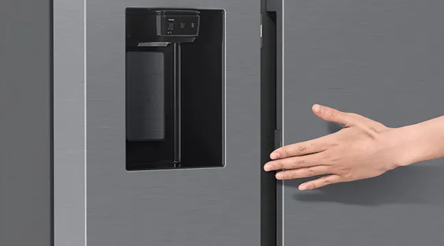 Una mano abre la puerta gris de un refrigerador con dispensador de agua y hielo negro empotrado.