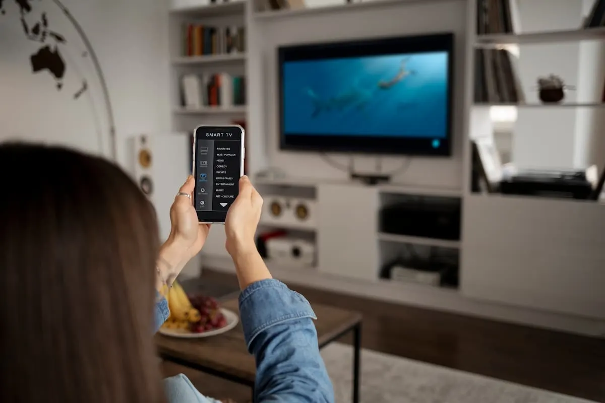 Persona controlando un televisor desde el móvil en una sala de estar.