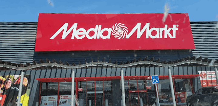 Edificio de Media Markt con rótulo rojo y letras blancas. Entrada con puertas de cristal y señal de acceso para discapacitados.
