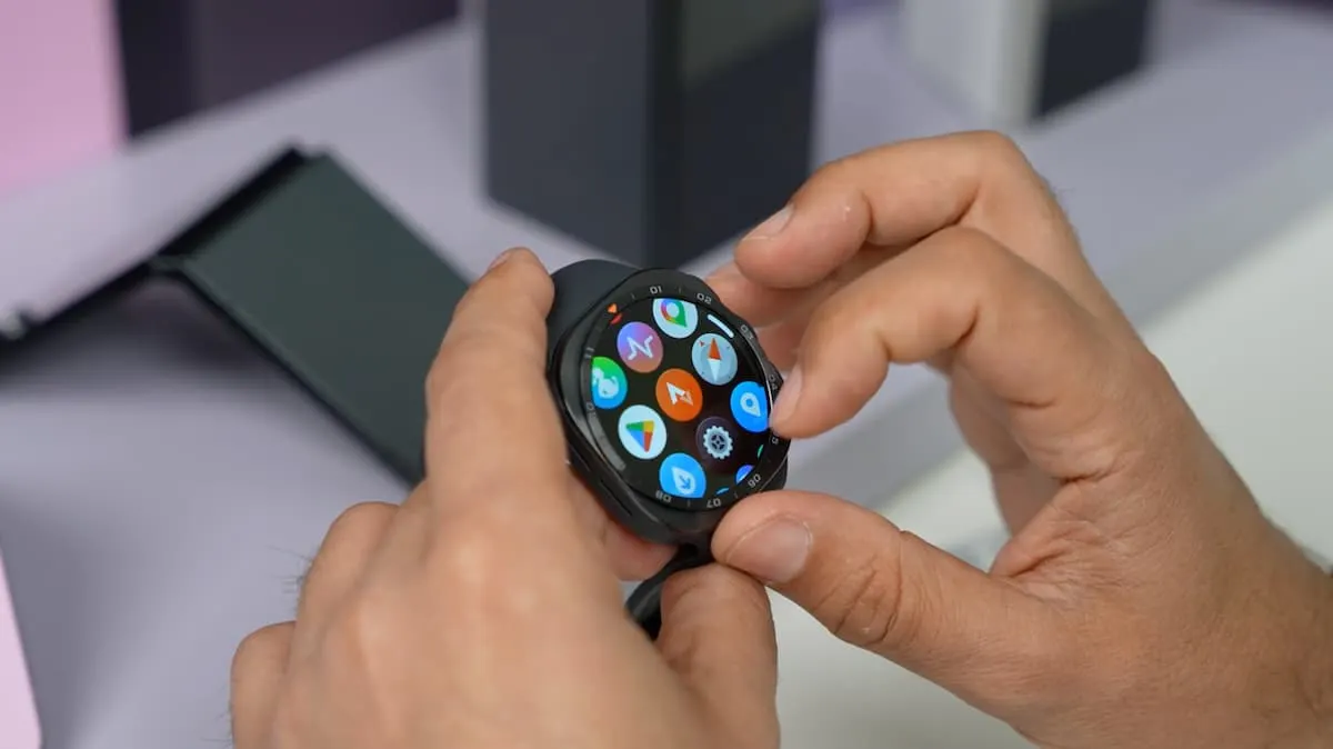 Manos sosteniendo un smartwatch Samsung Galaxy Watch con pantalla de apps encendida.