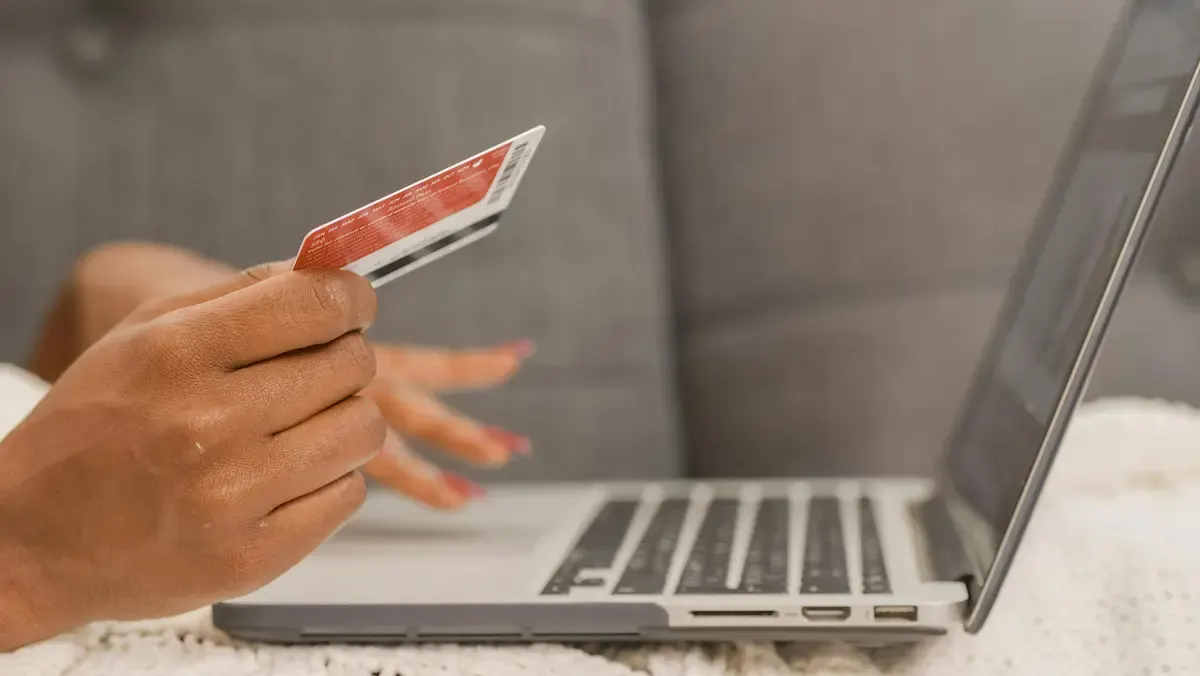 Una persona sostiene una tarjeta roja frente a una computadora portátil abierta sobre una superficie blanca texturizada.