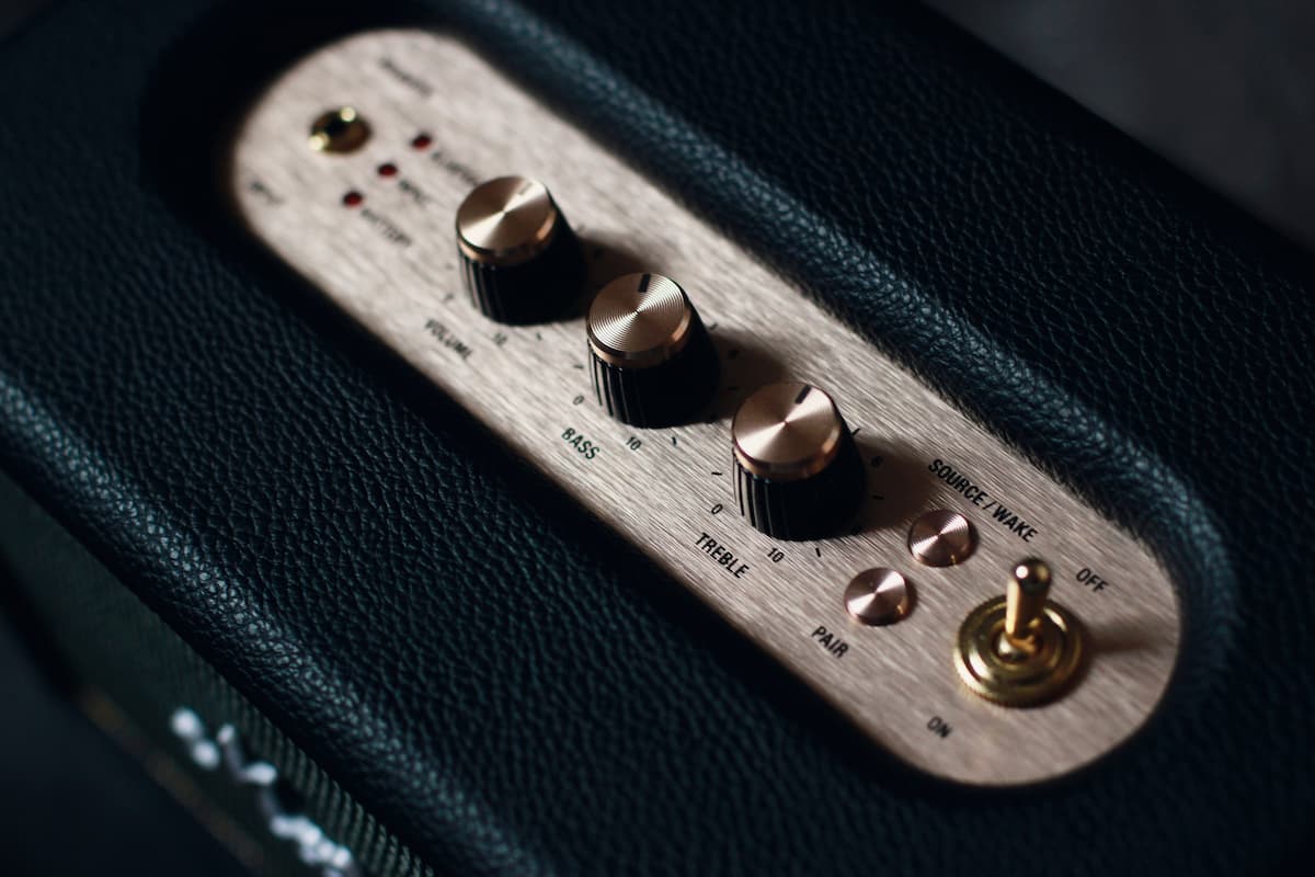 Primer plano de los controles de un altavoz Marshall verde con perillas doradas y panel de madera.
