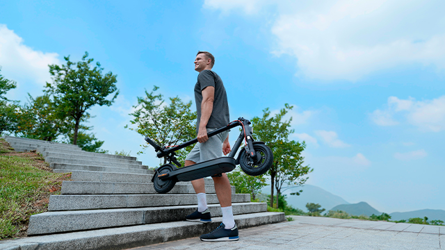 Persona cargando un Xiaomi Electric Scooter Elite plegado mientras sube unas escaleras al aire libre.