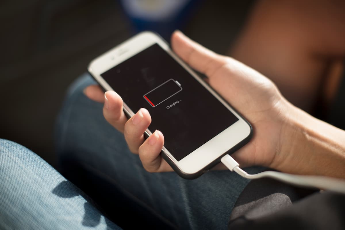 Mano sosteniendo un smartphone con icono de batería baja conectado a cargador