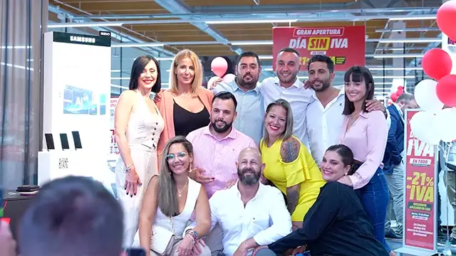 Grupo de personas posando frente a un cartel de "Día sin IVA" con globos rojos y blancos en una tienda.
