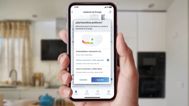 Smart phone encendido mostrando la función asistente de energía de la App Home Connect Balay. Cocina con electrodomésticos en el fondo