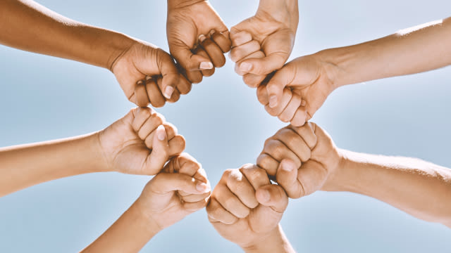 varias manos unidas formando una estrella contra un fondo blanco, simbolizando unidad o trabajo en equipo