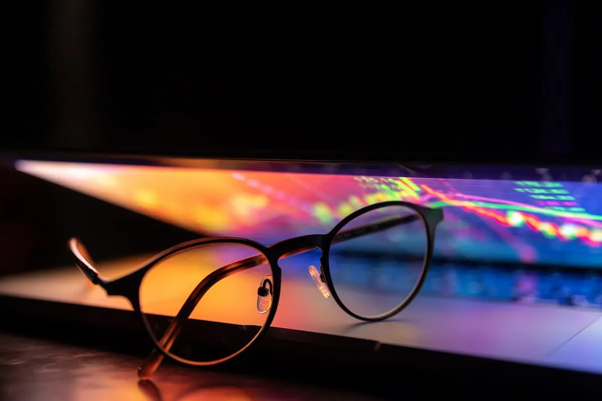 Gafas apoyadas sobre un portátil abierto con pantalla de colores brillantes y gráficos luminosos.