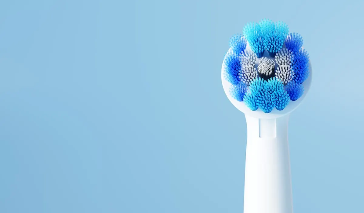 Cabezal de repuesto para cepillo de dientes eléctrico con cerdas azules y blancas dispuestas en forma circular, sobre fondo azul claro.