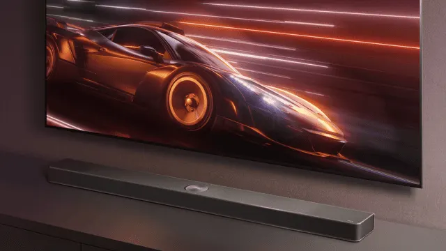 Televisor con imagen de coche deportivo y estela de luces, sobre una barra de sonido gris sobre mueble en ambiente oscuro.