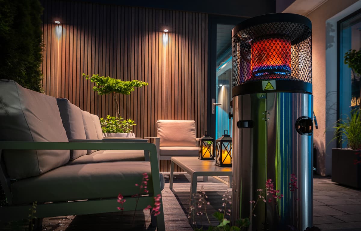 Estufa infrarrojos exterior encendida junto a un sofá exterior en un patio iluminado de noche.