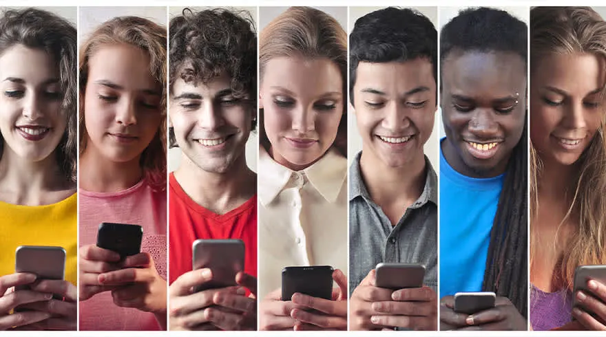 Siete personas sonriendo y mirando sus teléfonos móviles. Los individuos llevan ropa de diferentes colores.