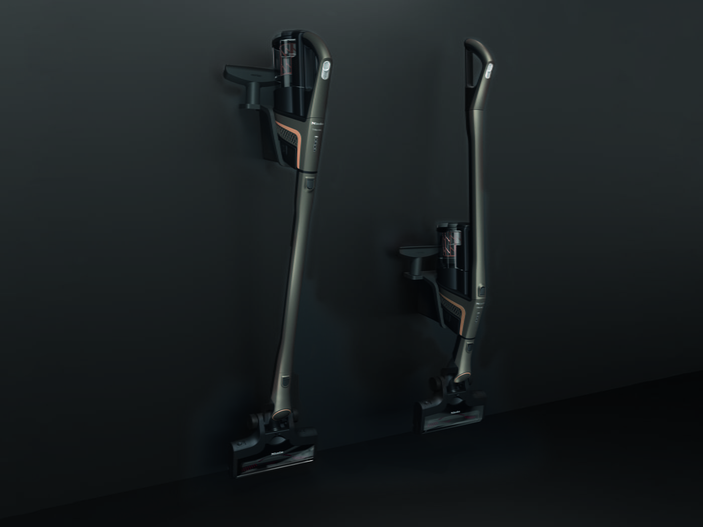 Dos aspiradoras verticales grises y negras están montadas en una pared gris oscuro. Una está extendida y la otra compacta.