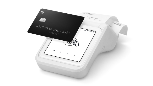 Tarjeta oscura sobre terminal de pago blanco con pantalla táctil. Un icono de pago inalámbrico se muestra en la tarjeta.