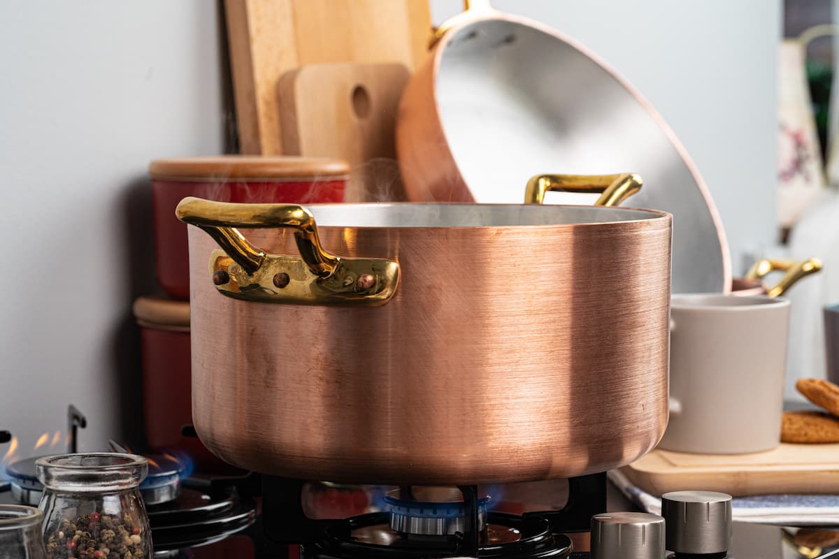 Olla de cobre con asas doradas sobre fogón de gas en cocina.