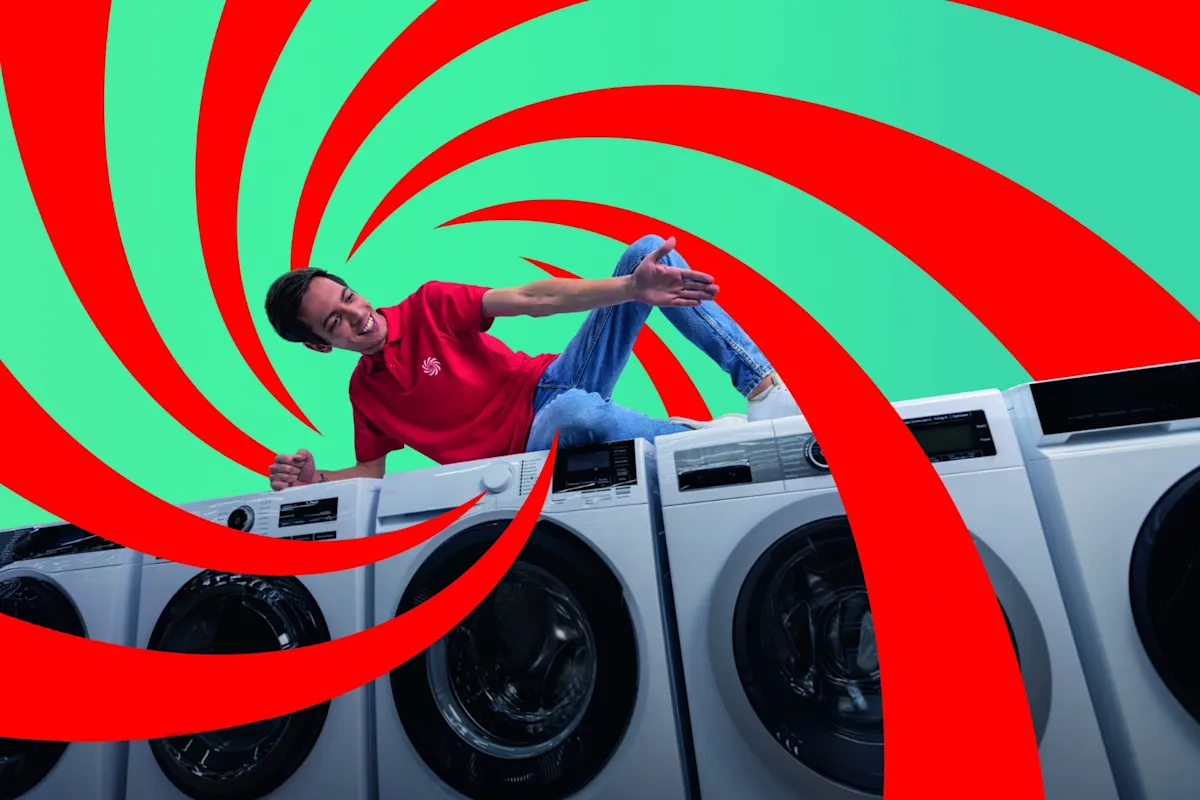 Un hombre con camisa roja y vaqueros está tumbado sobre varias lavadoras blancas. El fondo es verde con espirales rojas.