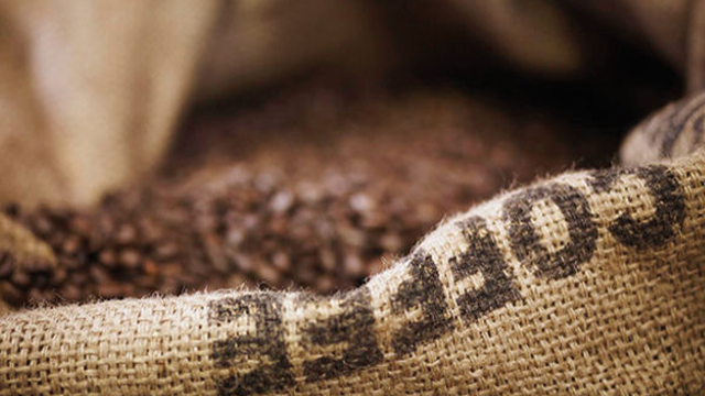 Saco de arpillera lleno de granos de café tostados. La palabra "COFFEE" es visible en el saco.