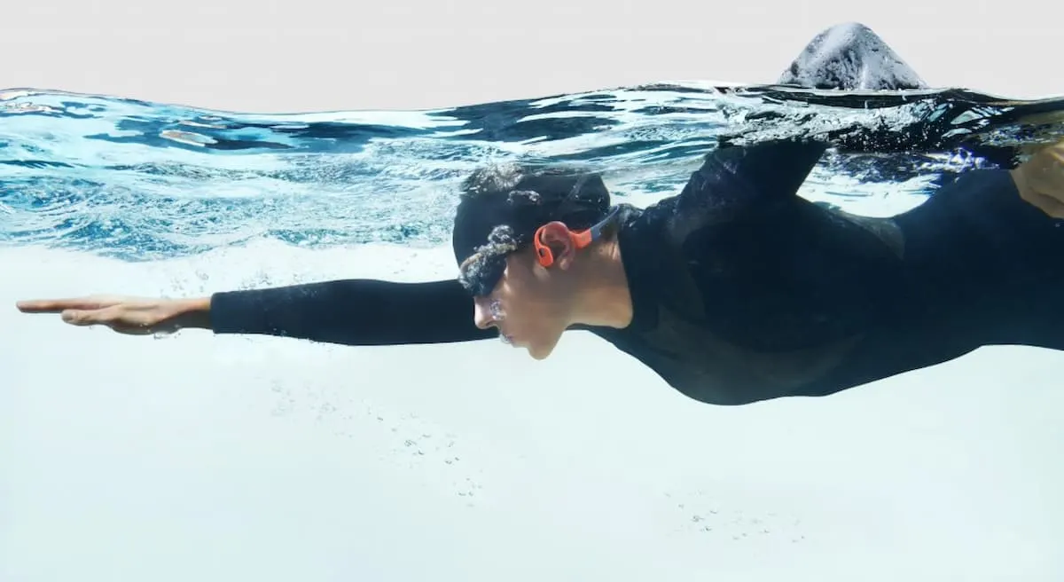 Nadadora de perfil avanzando bajo el agua con traje de neopreno.