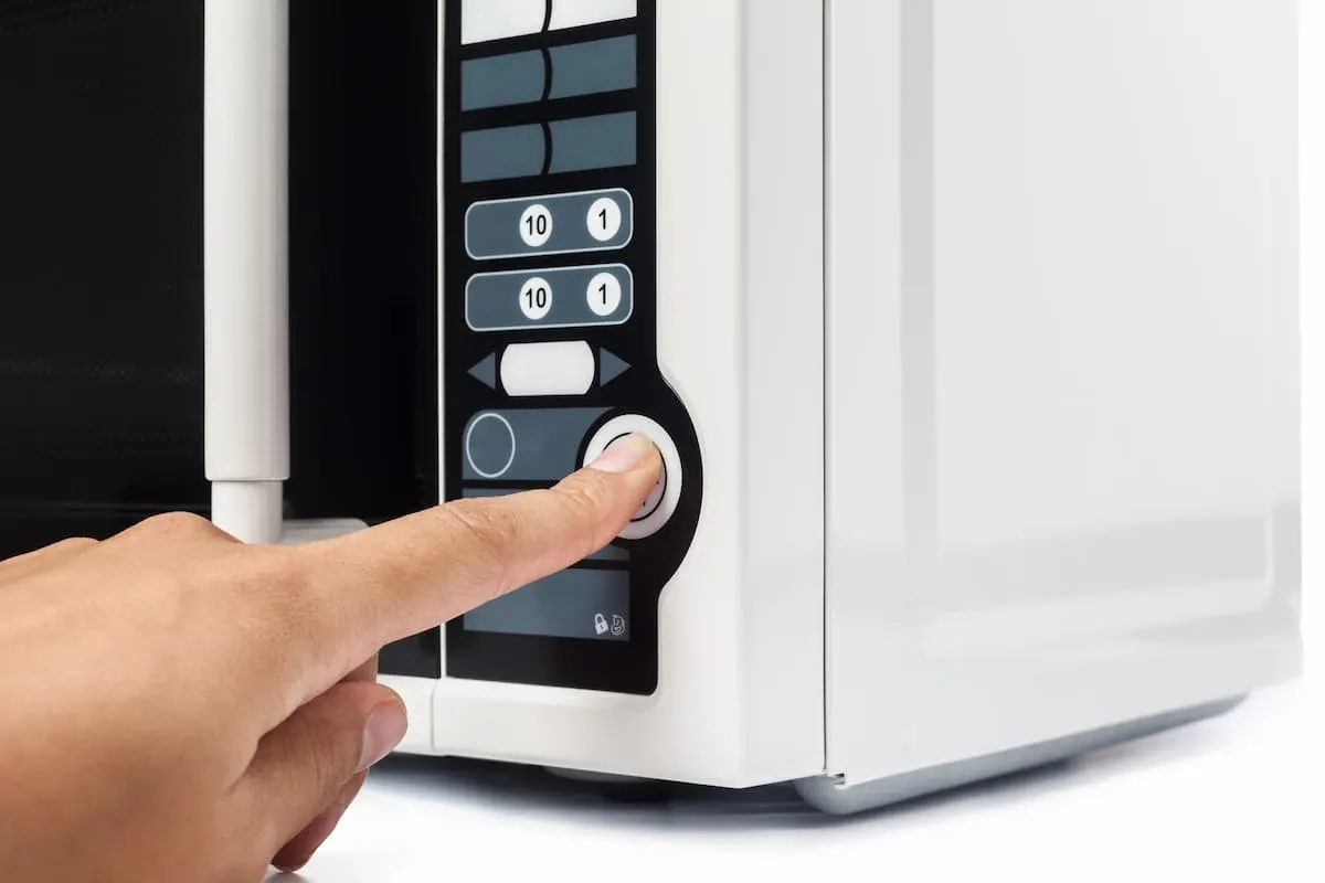 Mano pulsando el botón de encendido en el panel de un microondas blanco.