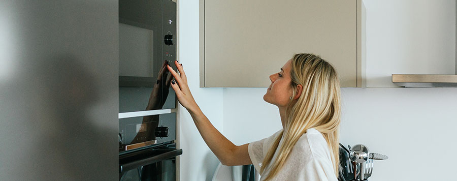 Una mujer en una cocina toca un horno negro. Hay armarios blancos en la pared.