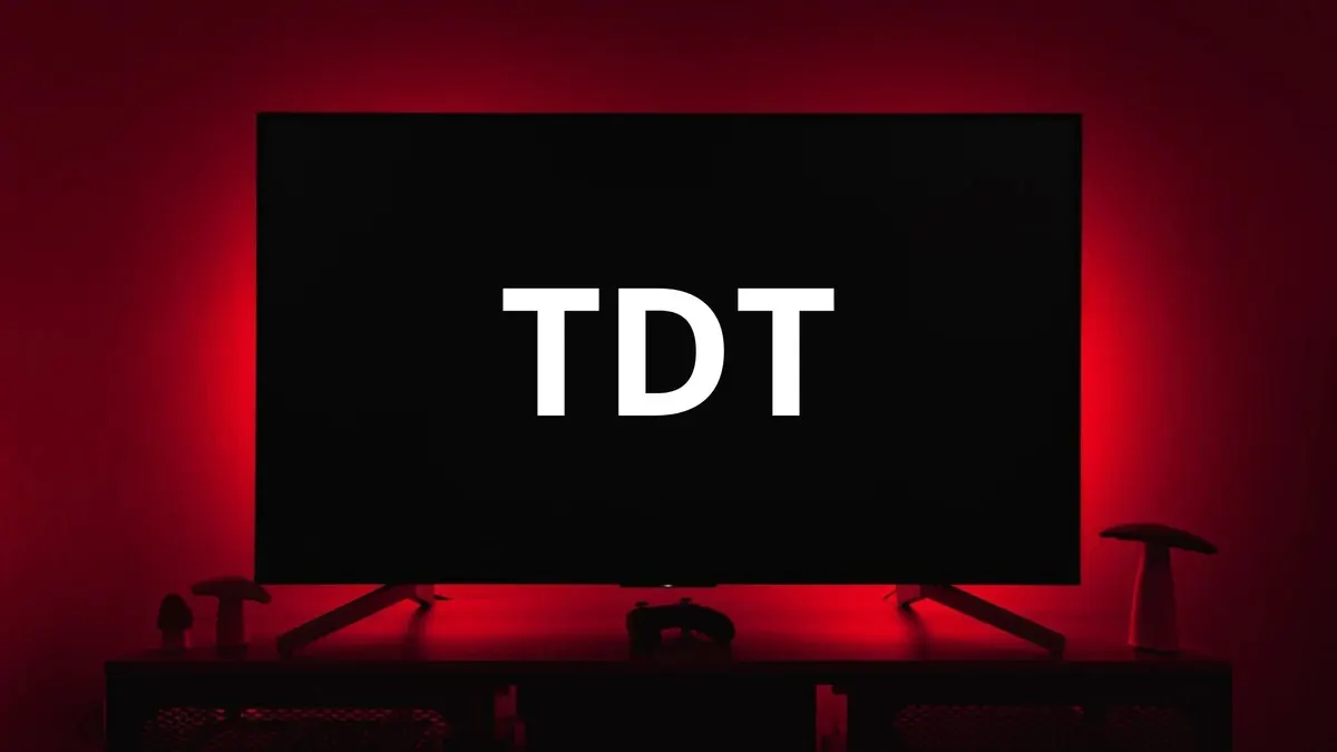 Televisor con la palabra "TDT" en blanco sobre un fondo negro, iluminado con luces rojas, sobre un mueble con objetos.