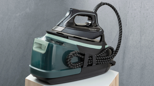 Mano sosteniendo varilla metálica con gránulos blancos, insertándola en agujero dorado de aparato gris y negro. Fondo blanco y beige.