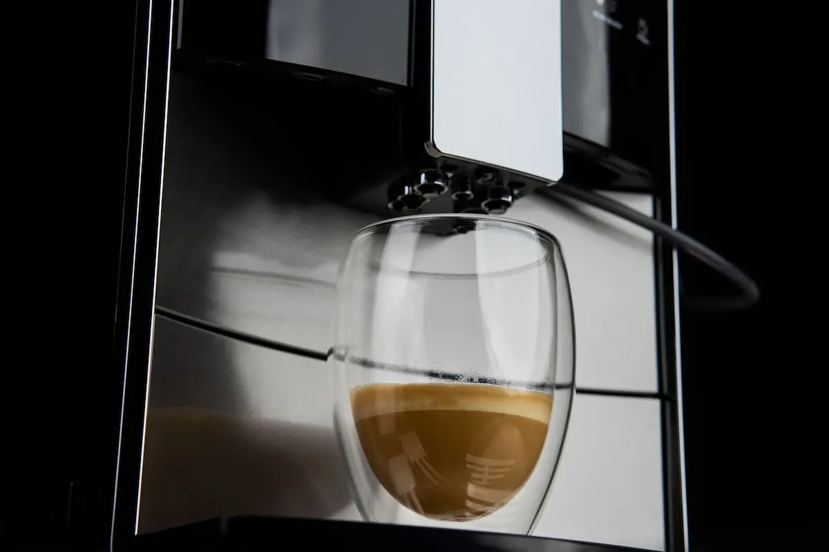 Vaso de doble pared colocado bajo el surtidor de una cafetera automática de acero inoxidable mientras se llena con un espresso cremoso.