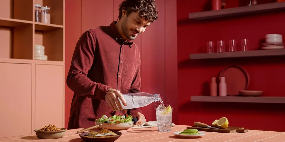 Hombre sirviendo agua con gas SodaStream en un vaso con hielo y lima
