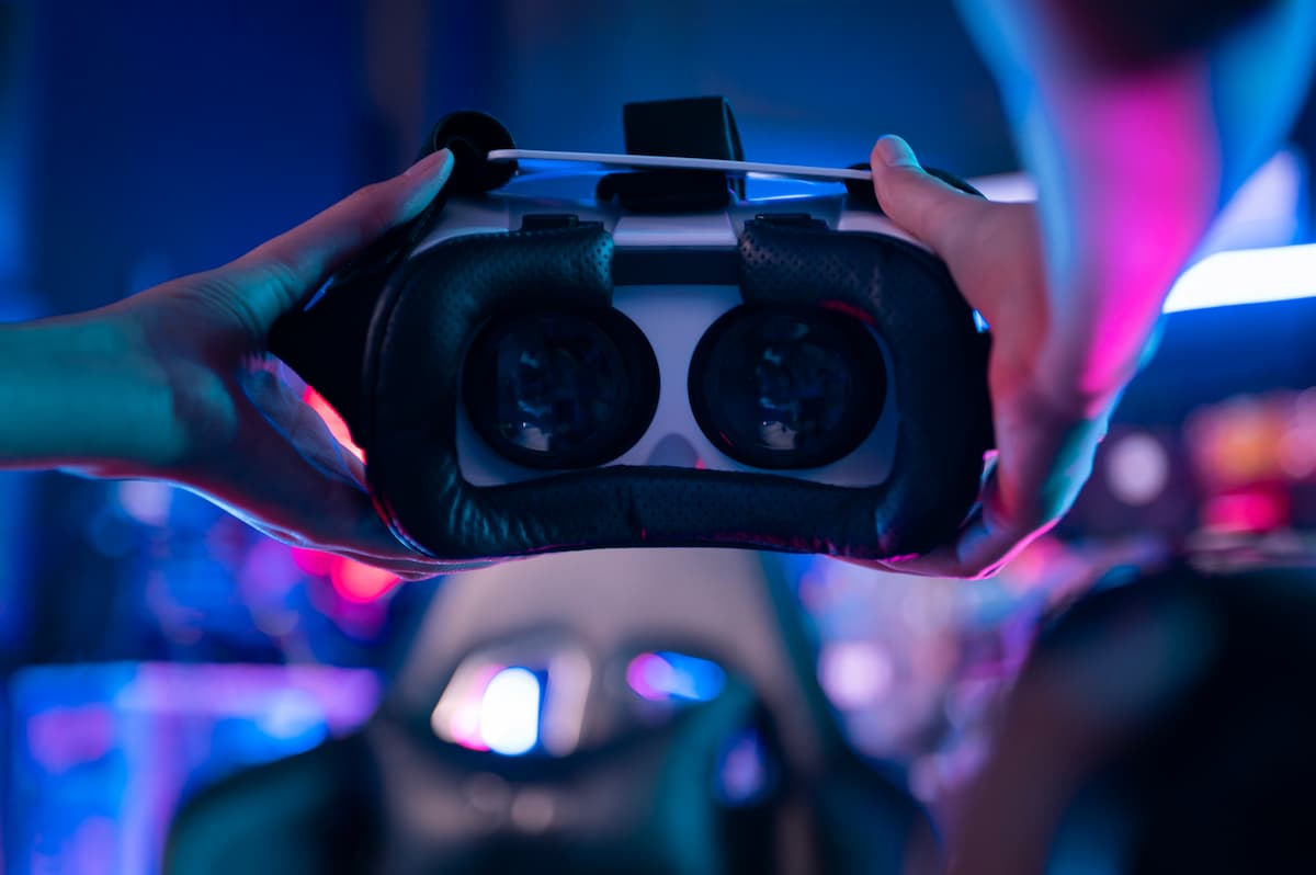 Manos sosteniendo unas gafas de realidad virtual con luces azules y rosas de neón de fondo.