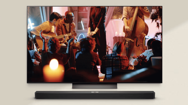 En un televisor se ven músicos tocando instrumentos frente a una audiencia, con una barra de sonido negra debajo.