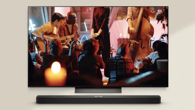 En un televisor se ven músicos tocando instrumentos frente a una audiencia, con una barra de sonido negra debajo.