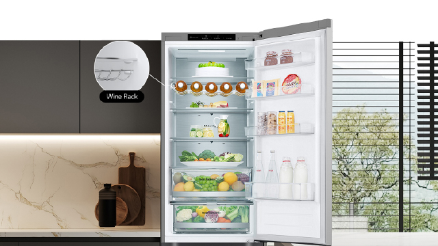 Frigorífico abierto con estantes llenos de comida: frutas, verduras y bebidas. En el fondo, una ventana con persianas.