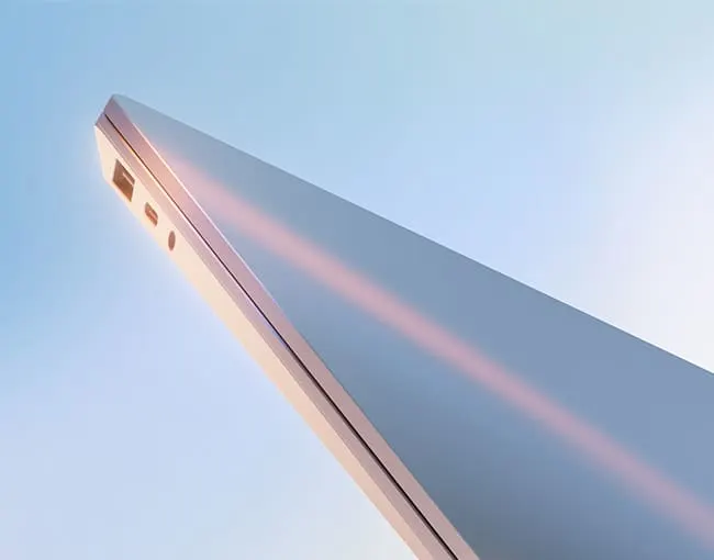 Vista en ángulo de un portátil plateado con puertos visibles contra un fondo azul claro.