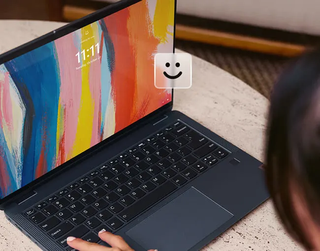 Un portátil abierto muestra una pantalla con un diseño colorido y la hora 11:11. Una persona usa el teclado. Fondo beige.