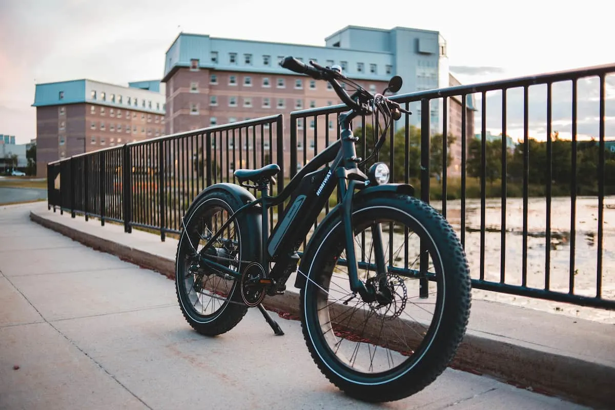 Bicicleta eléctrica negra aparcada junto a una barandilla urbana.