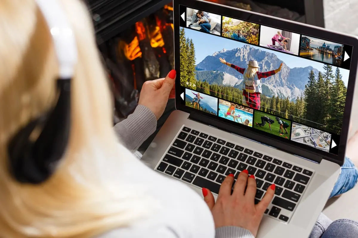 Mujer con auriculares revisando fotos de vacaciones en su portátil, con una chimenea de fondo.