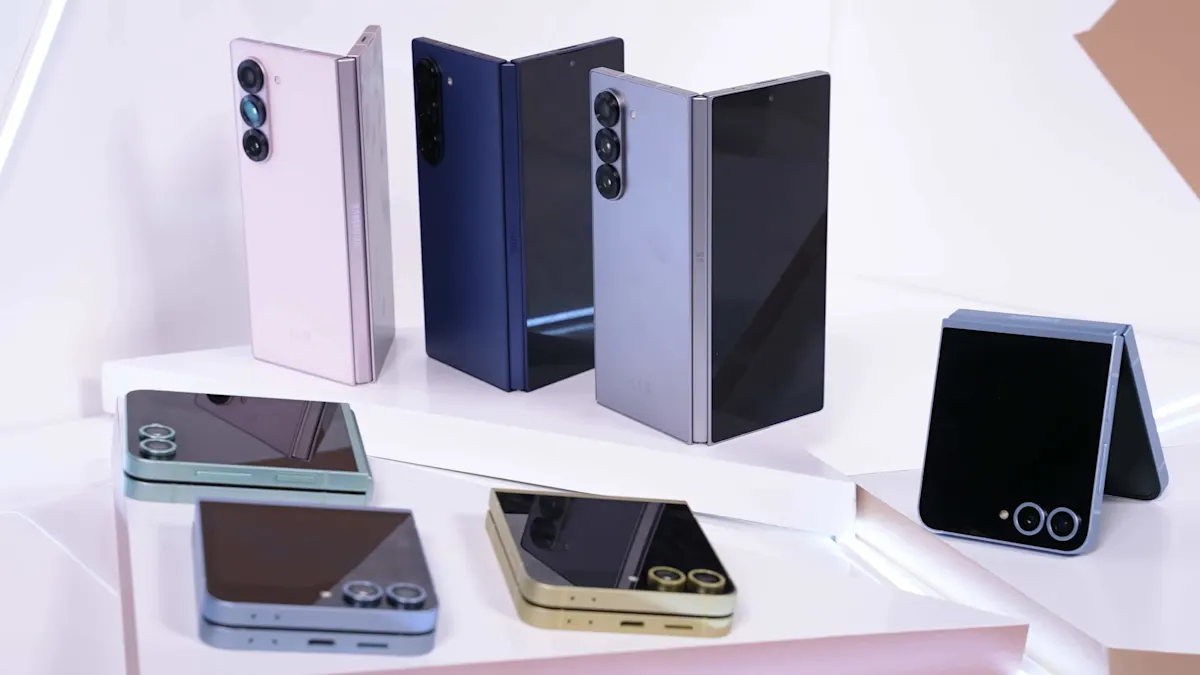 Varios teléfonos plegables en tonos rosa, azul, gris y dorado sobre una superficie blanca con detalles geométricos.