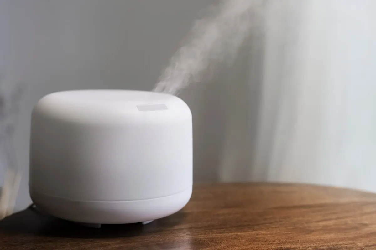 Difusor de aroma blanco emitiendo vapor sobre una mesa de madera.