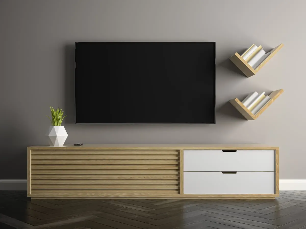 Televisor de pantalla plana montado en la pared sobre un mueble bajo de madera, con dos estanterías diagonales a la derecha.
