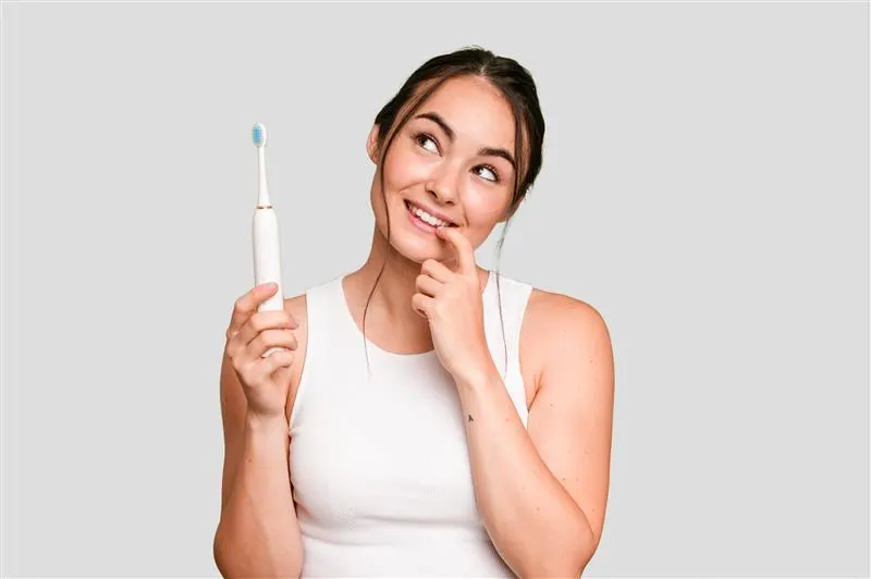Mujer joven sosteniendo un cepillo dental eléctrico y sonriendo.