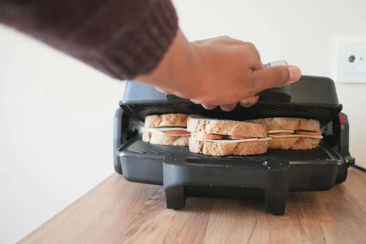 Persona usando una sandwichera con sándwiches de pan integral.
