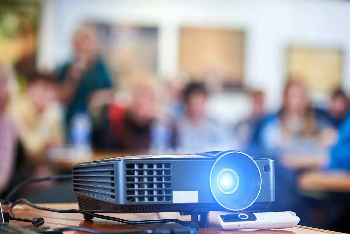 Proyector encendido en primer plano con audiencia desenfocada al fondo en una sala de conferencias.