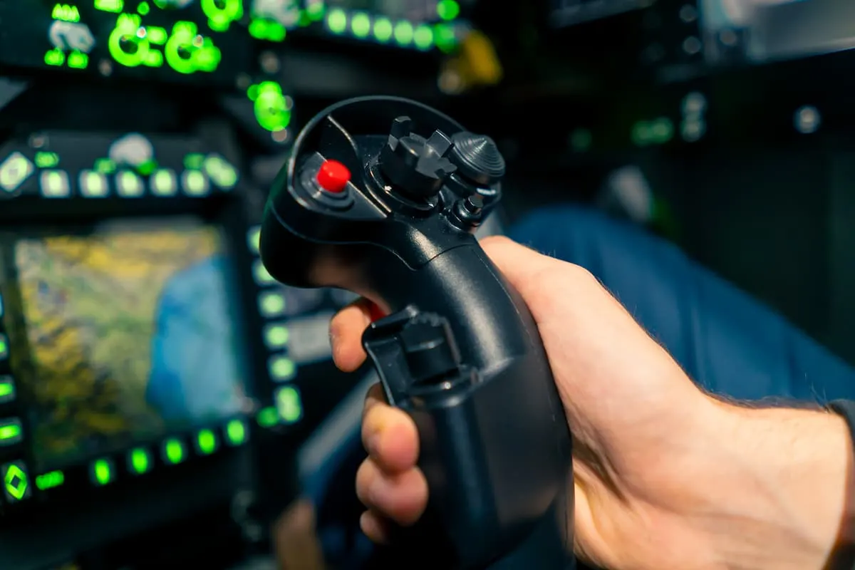 Mano sujetando un joystick de control en una cabina llena de pantallas y luces verdes